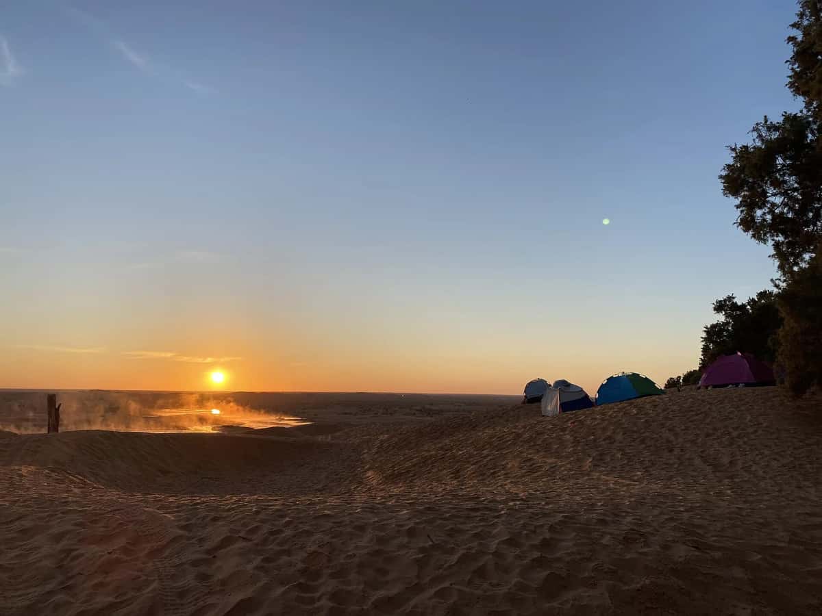 Tentes d'un bivouac au coucher du soleil sur les dunes, près de Ksar Ghilane