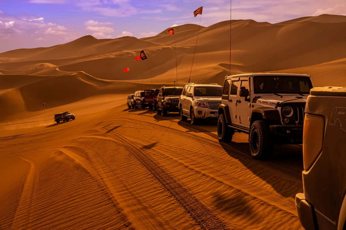 Convoi de 4x4 dans de grandes dunes de sable au coucher du soleil