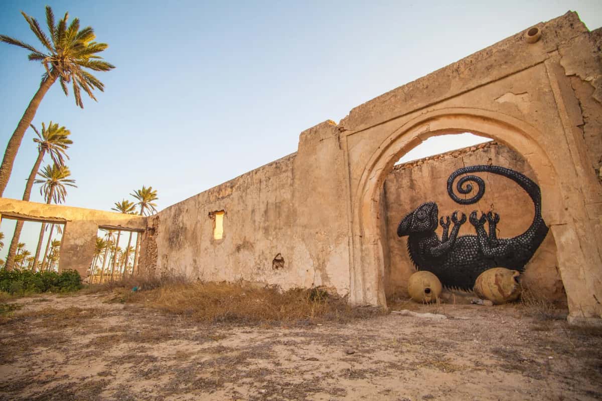 Caméléon noir de l'artiste ROA peint sous une arche en ruine à Erriadh, Djerbahood, Djerba
