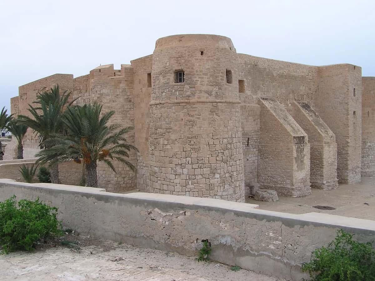 Tour ronde et remparts en pierre du fort Ghazi Mustapha, ou Borj El Kebir, entre les palmiers à Houmt Souk, Djerba
