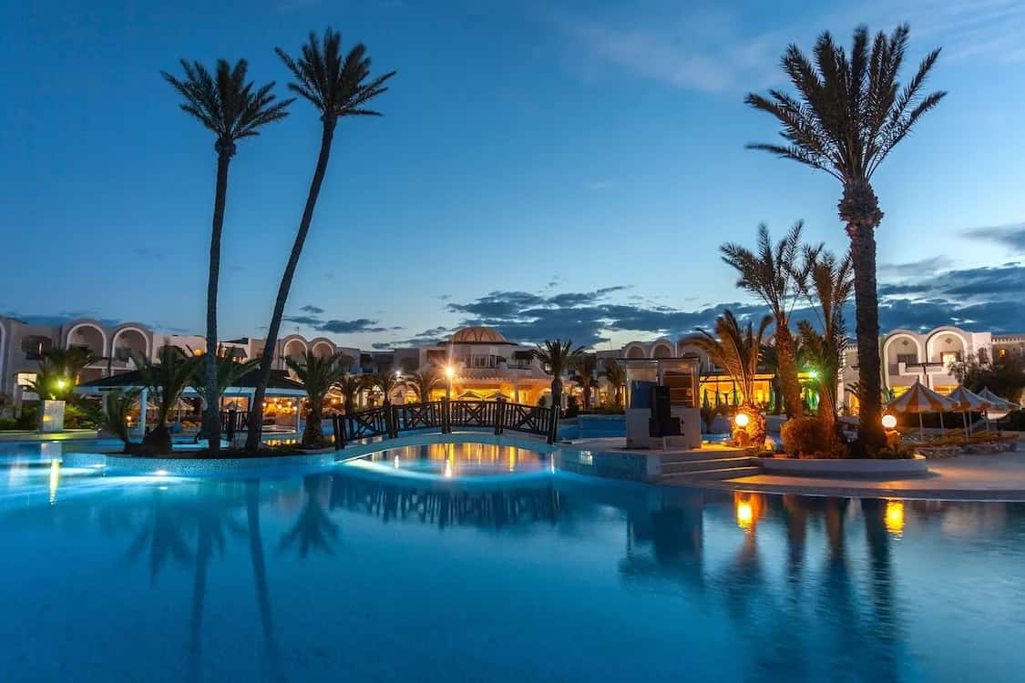 Piscine éclairée au crépuscule entourée de palmiers à l'hôtel Djerba Holiday Beach (Club Framissima) à Mezraia
