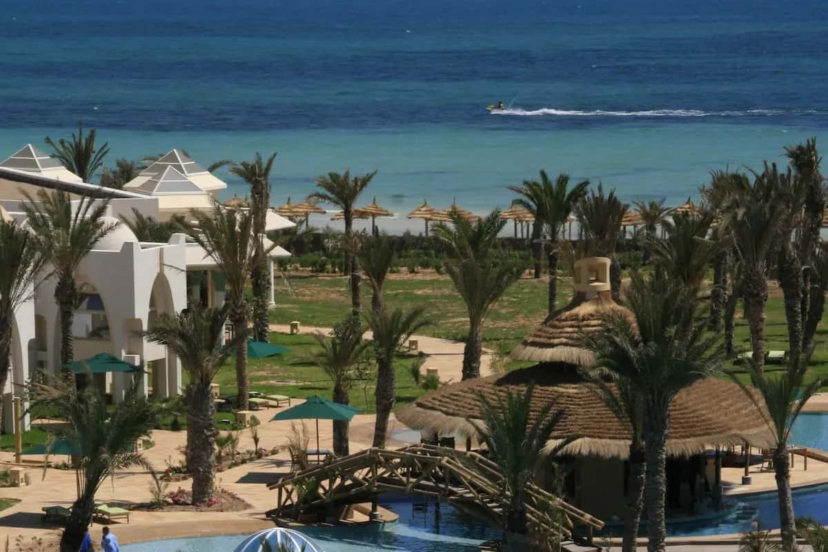 Piscines, pont en bois et bar de plage au toit de chaume de l'hôtel Hasdrubal Prestige Thalassa & Spa à Djerba, avec la mer en toile de fond