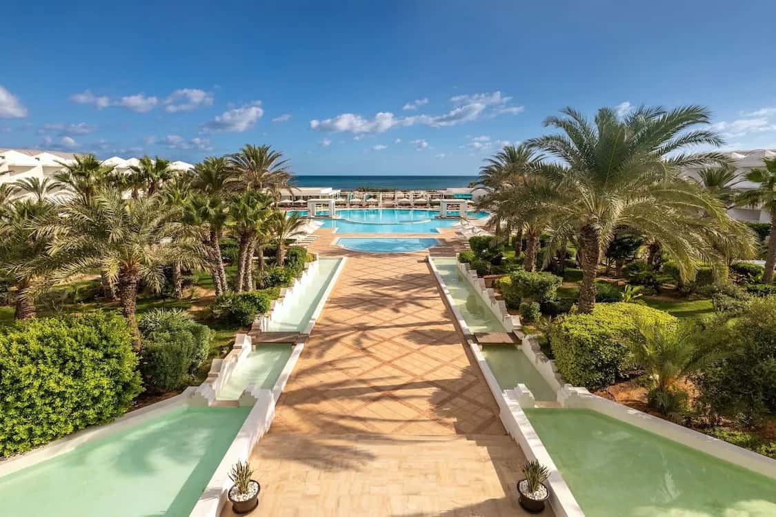 Allée de bassins et jardin de palmiers menant à la piscine et à la mer au Radisson Blu Palace Resort & Thalasso à Djerba