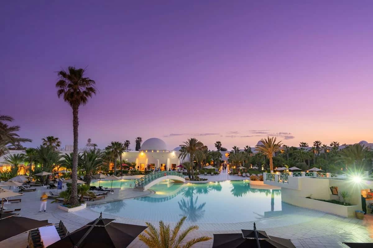Piscine éclairée et jardin de palmiers au crépuscule à l'hôtel Yadis Djerba Golf Thalasso & Spa à Midoun