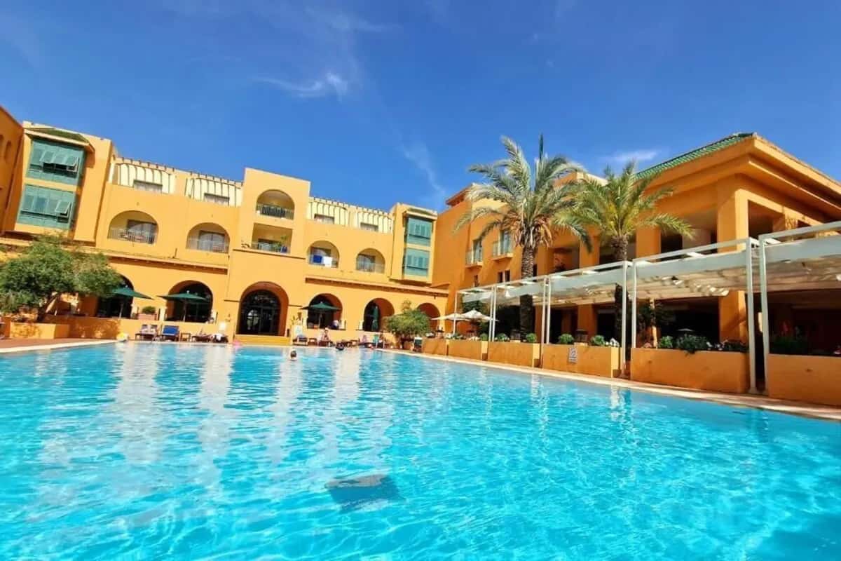 Grande piscine turquoise devant la façade ocre de l'hôtel Alhambra Thalasso à Yasmine Hammamet