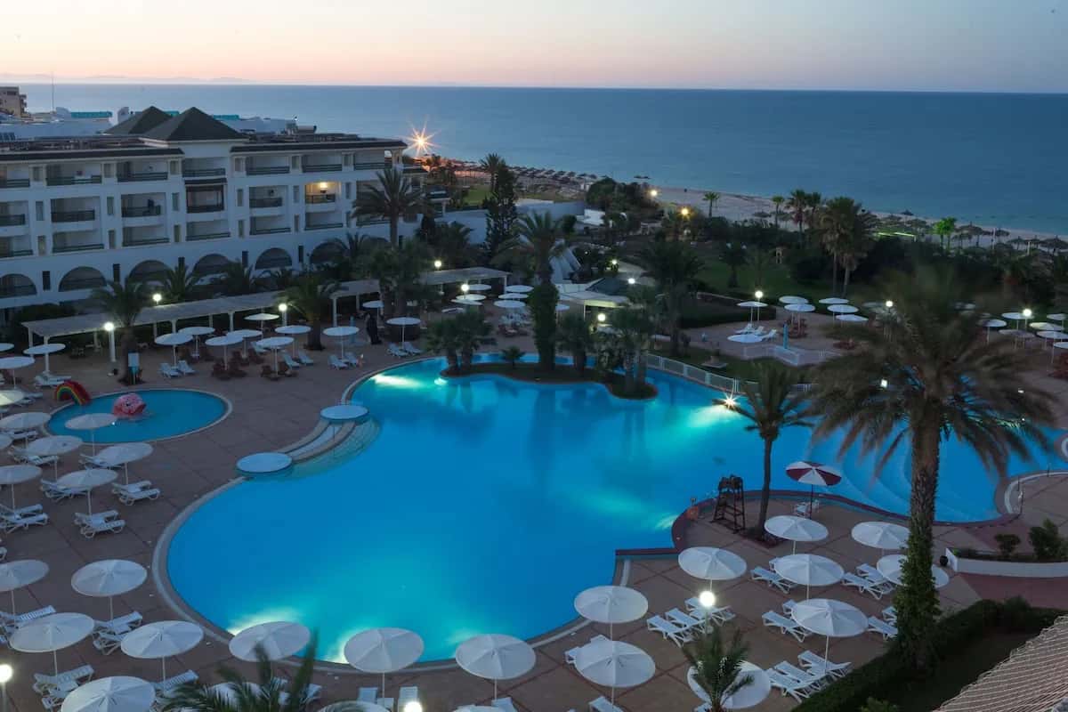 Piscine illuminée au crépuscule et façade de l'hôtel El Mouradi Palm Marina, Port El Kantaoui