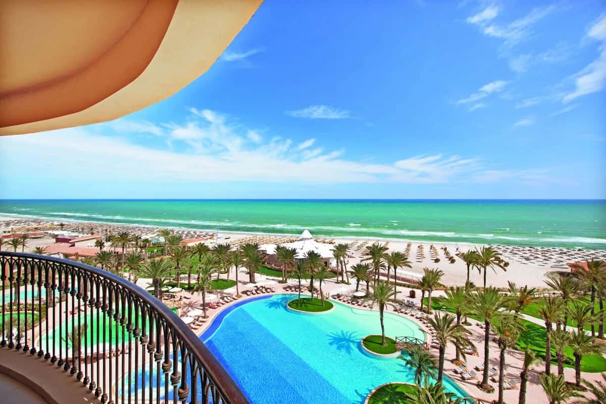 Piscines, palmiers et plage de sable vus depuis un balcon du Mövenpick Resort & Marine Spa à Sousse