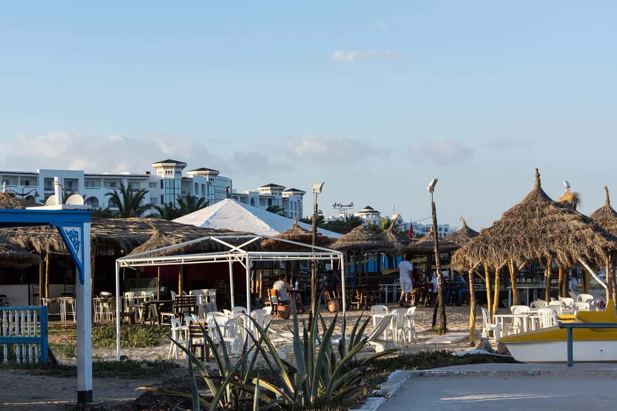 Hôtels aux bâtiments blancs en bord de plage à Yasmine Hammamet, avec paillotes et tables sur le sable au coucher du soleil