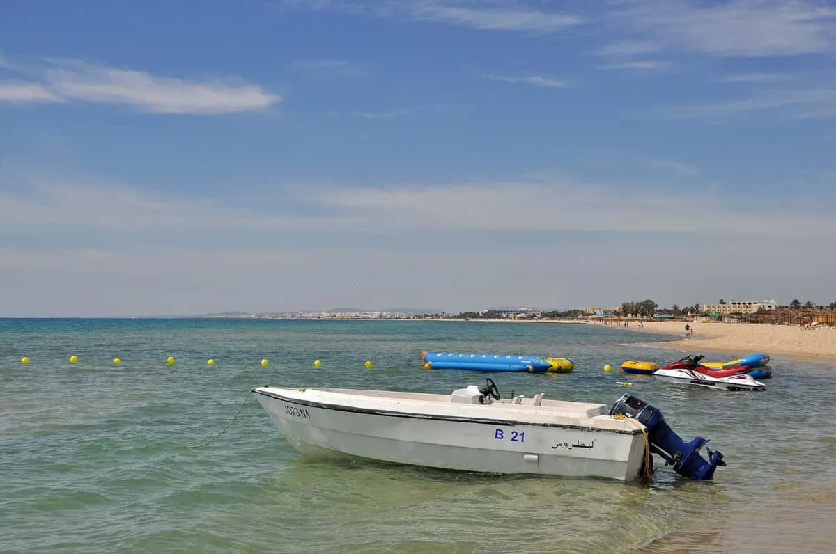 Plage du golfe de Hammamet, eau turquoise peu profonde et bateaux à moteur amarrés