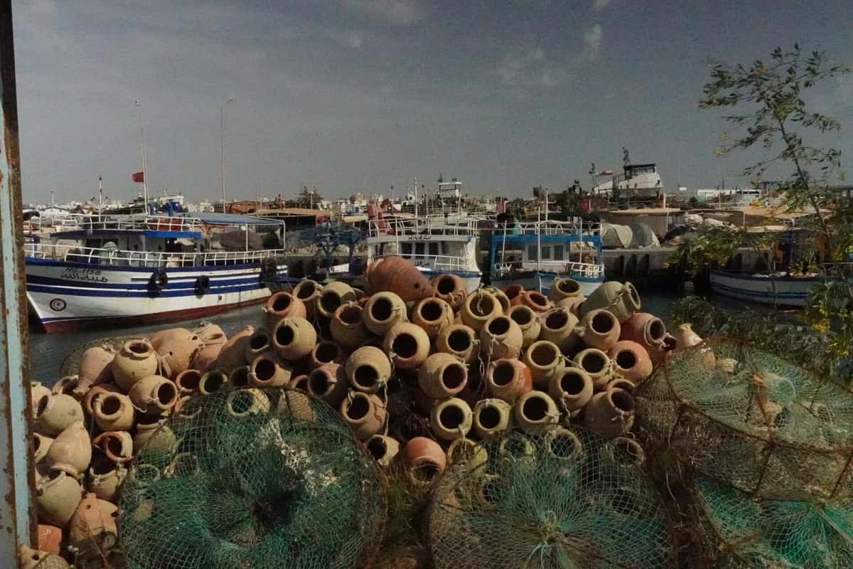 Chalutiers amarrés et pile de jarres à poulpes au port de pêche de Zarzis