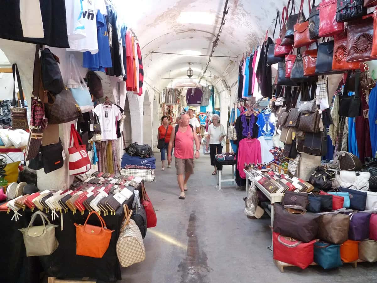 Ruelle voûtée du souk de Houmt Souk, bordée de sacs et de vêtements, à Djerba