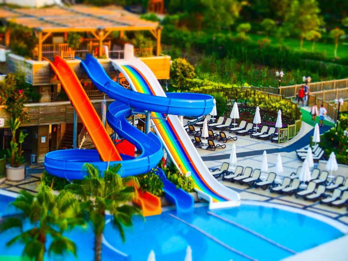 Toboggans colorés d'un parc aquatique au bord d'une piscine, entre palmiers et transats